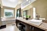 Dual-sink vanity with vessel basins, stone-finish countertop, dark cabinetry, and a deep soaking tub with tile surround