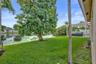 Backyard featuring a concrete patio with a white pergola, waterfront lot with mature trees, and a manicured lawn