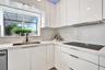 High-gloss white cabinetry, white stone-finish countertops, integrated stone-finish backsplash, undermount sink with gooseneck faucet, and built-in el
