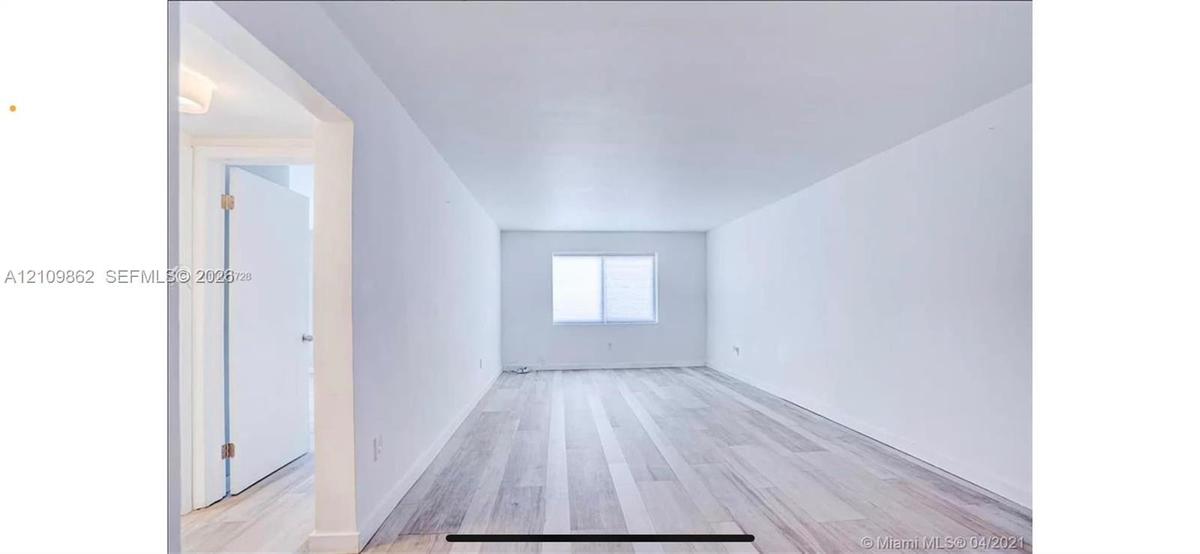 Neutral interior space featuring wood-finish flooring, a rectangular window, and a white door with a metal handle