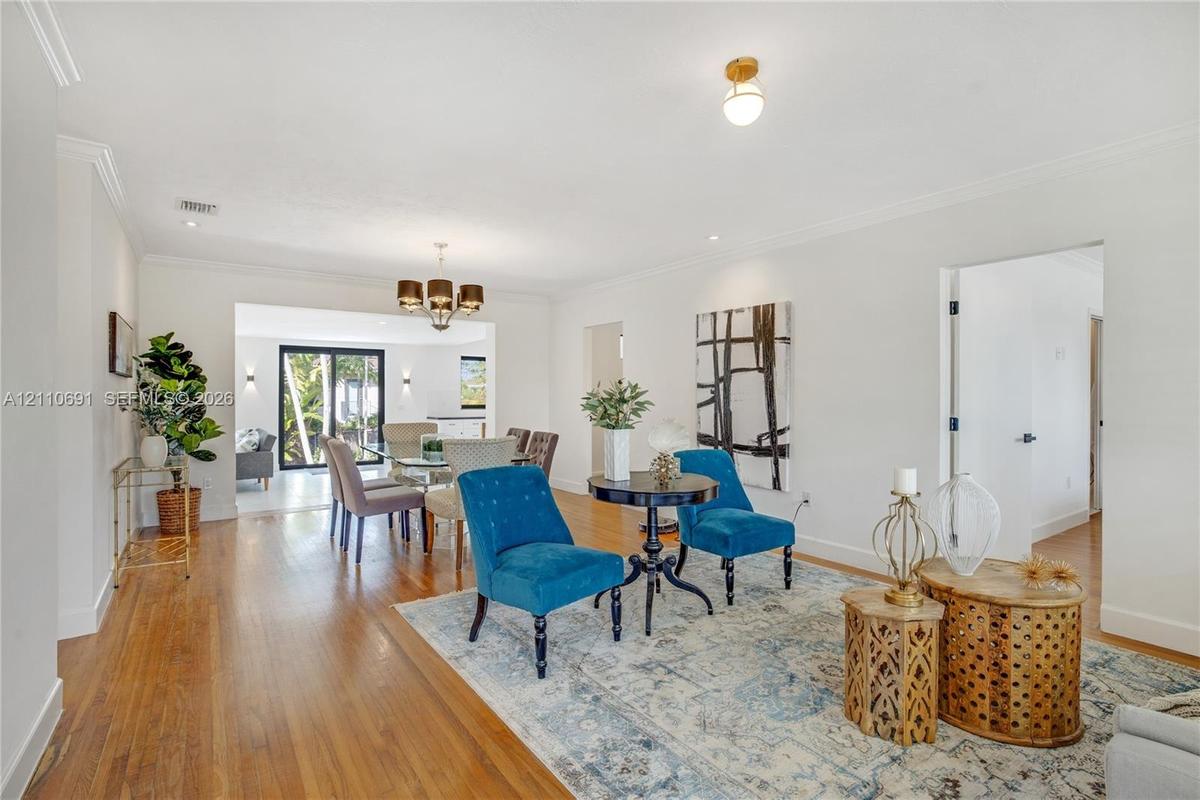 Open-concept interior featuring wood-finish flooring, crown molding, multi-arm chandelier lighting, and sliding glass doors