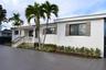 Stucco exterior featuring a covered front porch with a concrete balustrade, herringbone-patterned paved driveway, decorative shutters, and mature palm