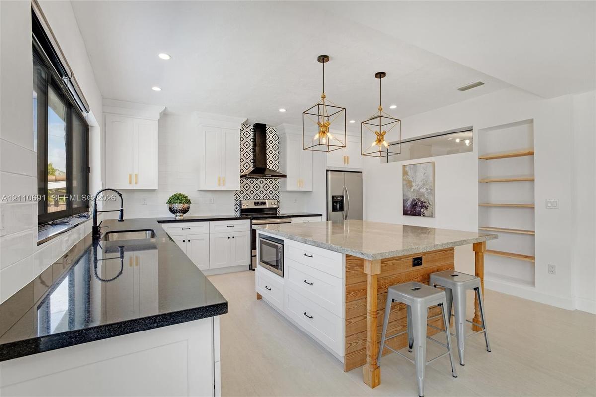 Kitchen featuring white shaker cabinetry, black stone countertops, geometric tile backsplash, central island with wood paneling, and open built-in she
