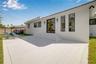 Rear exterior featuring a herringbone-patterned paved patio, white stucco siding, sliding glass doors, vertical rectangular windows, and exterior wall
