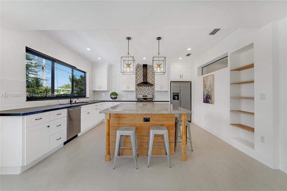 Kitchen featuring a center island with wood-finish cabinetry, stone countertop, geometric metal pendant lighting, patterned tile backsplash, and built