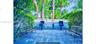 Outdoor patio area featuring square stone pavers, two built-in charcoal grills, and perimeter white picket fencing surrounded by mature trees and gree