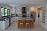 Kitchen featuring white shaker cabinetry, stone-topped central island with wood paneling, geometric tile backsplash, recessed lighting, and built-in s