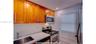 Kitchen featuring wood cabinetry, white countertops, textured white tile backsplash, stainless steel appliances, and a single-basin undermount sink