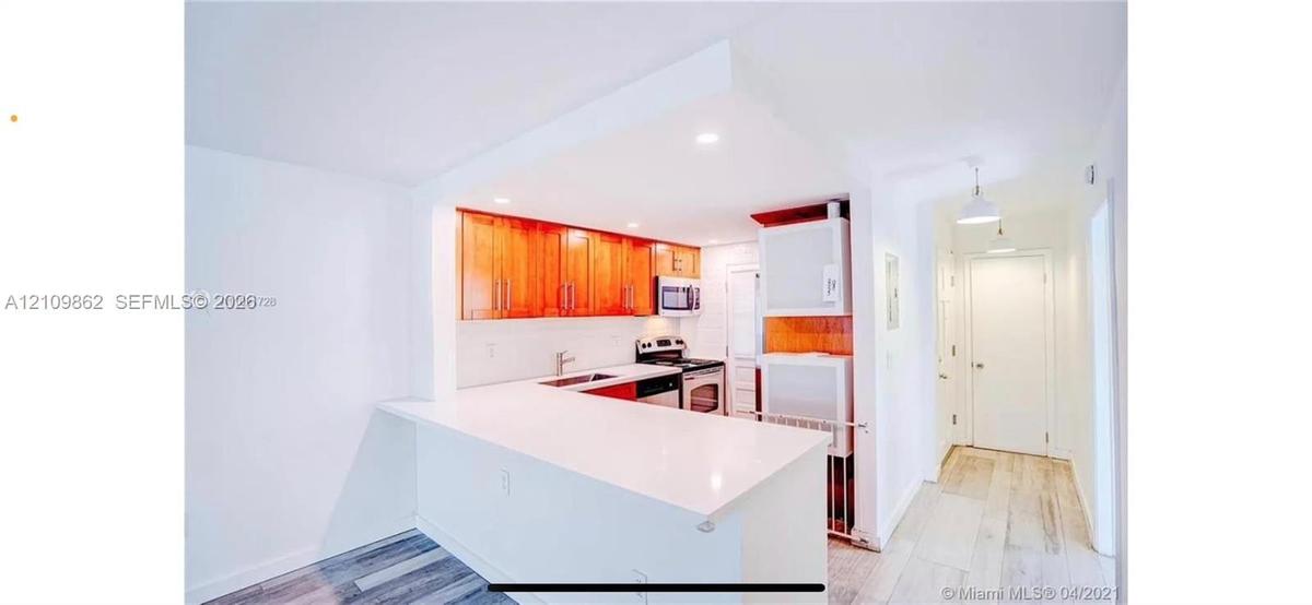 Kitchen featuring wood-finish cabinetry, white solid-surface countertops, integrated stainless steel appliances, recessed ceiling lighting, and wood-f