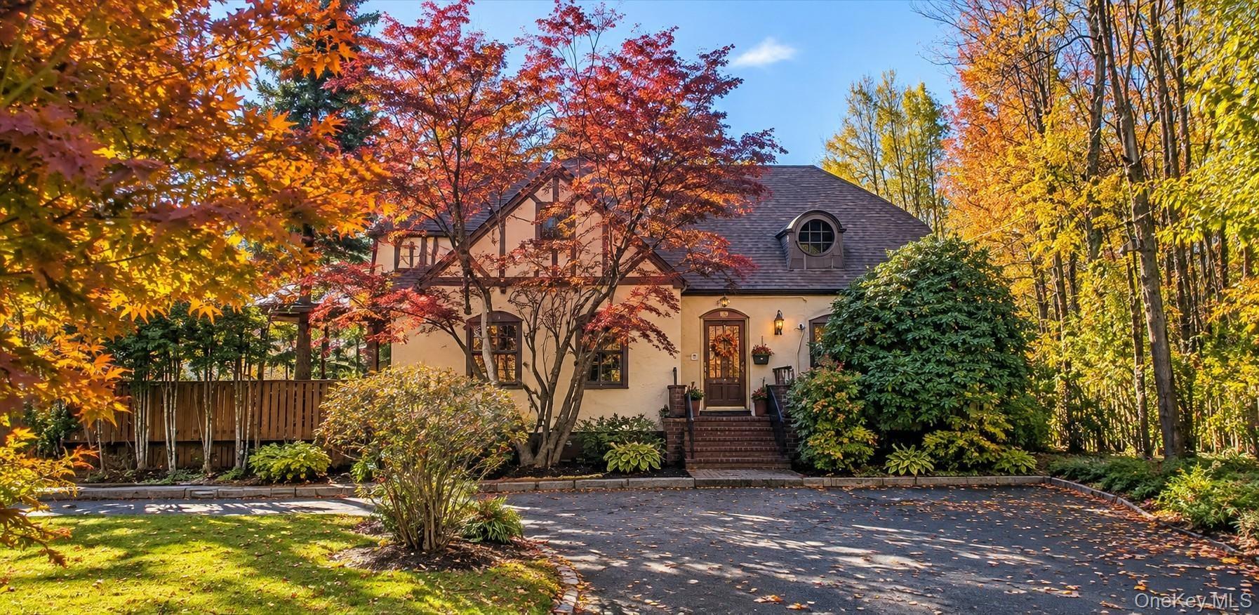 Tudor-style exterior featuring stucco facade with half-timber detailing, prominent gable roofline, arched dormer window, and brick entry steps