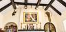 Vaulted ceiling featuring exposed dark-toned beams, textured plaster walls, built-in arched shelving, and track lighting
