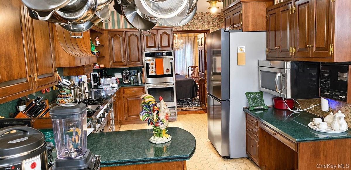 Kitchen featuring raised-panel wood cabinetry, integrated double wall ovens, a gas cooktop, solid-surface countertops, and a ceiling-mounted pot rack