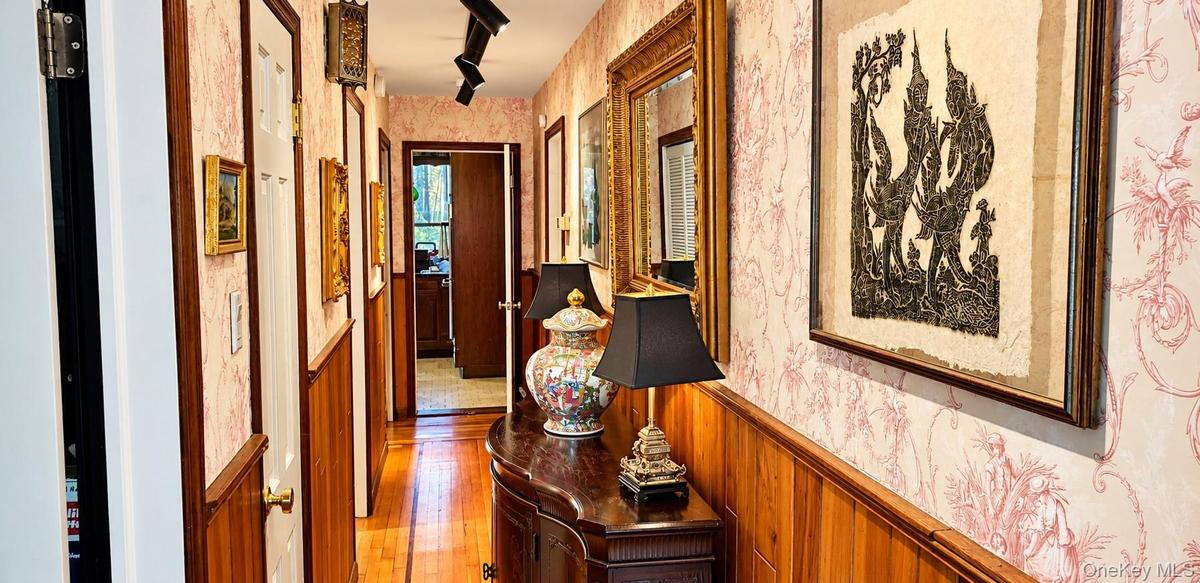 Hallway featuring patterned wallpaper, horizontal wood wainscoting, wood-finish flooring, and adjustable track lighting