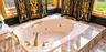 Jetted oval soaking tub featuring a natural stone surround, polished gold-tone hardware, and integrated gold-tone grab bars