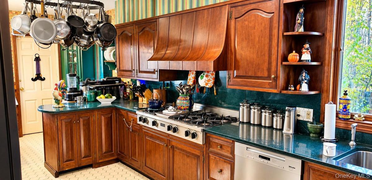 Kitchen featuring custom wood cabinetry, a decorative wood range hood, integrated stainless steel appliances, a multi-burner gas cooktop, and polished