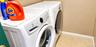 White front-loading laundry appliances featuring digital control panels and integrated glass-front doors, set against a neutral wall finish and hexago
