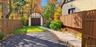 Tudor-style detached garage with stucco and timber detailing, paved driveway, enclosed perimeter fencing, concrete walkway, and landscaped garden beds