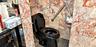 Bathroom featuring floor-to-ceiling multi-tonal red and grey stone tiling, black plumbing fixture, stainless steel wall-mounted grab bar, and dark-ton