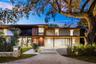 Modern multi-level exterior featuring wood-paneled siding, stone-finished masonry, expansive floor-to-ceiling glass windows, and a paved herringbone d