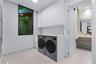 Laundry room featuring floor-to-ceiling cabinetry, custom solid-surface countertops, large-format tile flooring, and a window with natural foliage exp