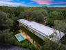 Modern two-story structure featuring a flat roofline, minimalist facade, in-ground swimming pool, expansive hardscaped patio, and mature perimeter lan