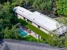 Modern residence featuring a flat roof with integrated skylights, a sprawling covered terrace with an artificial turf canopy, and a private swimming p