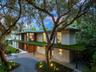 Modern architectural exterior featuring a flat roofline, horizontal stone and wood siding, integrated green roof canopy, gravel motor court, and linea