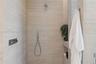 Walk-in shower featuring large-format textured stone wall tile, built-in shelving, a rainfall showerhead, and a wall-mounted handheld shower fixture w