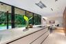 Modern kitchen featuring a stone-topped island, floor-to-ceiling glass panel walls, integrated ceiling lighting, and wood-finish cabinetry