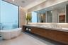 Floating wood-finish vanity with dual integrated sinks, light-toned stone countertop, freestanding soaking tub, expansive wall-to-wall mirror, and rec