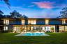 Modern two-story architectural exterior featuring expansive glass walls, a covered patio with recessed lighting, a rectangular in-ground pool, and woo