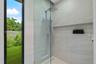 Walk-in shower featuring floor-to-ceiling stone-finish tile, frameless glass enclosure, rainfall shower head, handheld sprayer, and an integrated rece