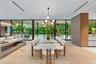 Floor-to-ceiling glass walls, wood-finish flooring, linear recessed lighting, integrated wall cabinetry, and a contemporary multi-arm chandelier