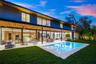 Modern two-story exterior featuring expansive floor-to-ceiling glass wall systems, a recessed wood-paneled ceiling, a rectangular in-ground swimming p