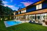 Modern architectural exterior featuring expansive wood-paneled eaves, full-height sliding glass walls, a covered concrete patio, and an in-ground swim