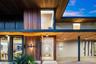 Contemporary facade featuring extensive wood-paneled cladding, floor-to-ceiling glass windows, recessed ceiling lighting, a wide pivot entry door, and