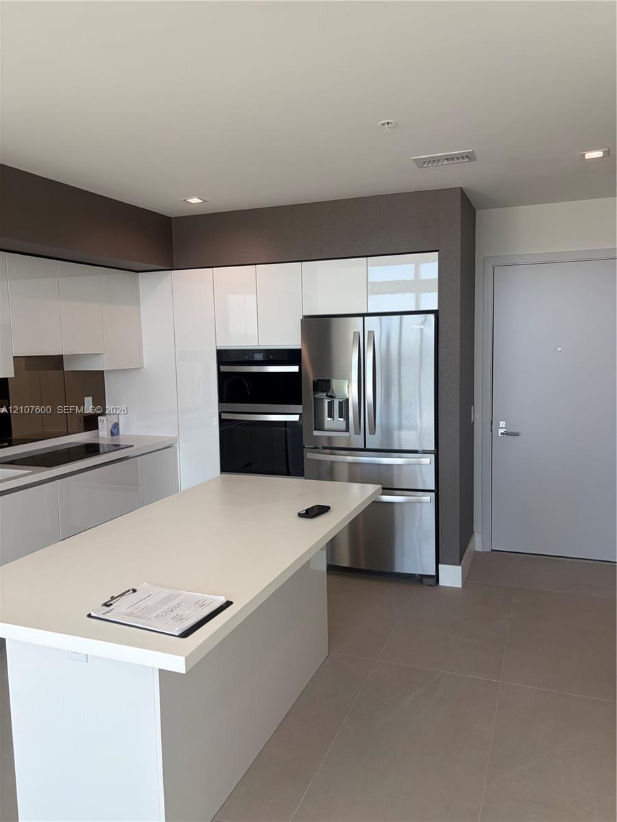 Kitchen featuring a central island with a solid surface countertop, high-gloss white cabinetry, stainless steel appliances including a built-in wall o