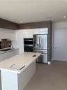 Kitchen featuring a central island with a solid surface countertop, high-gloss white cabinetry, stainless steel appliances including a built-in wall o