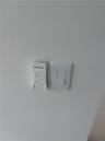 Wall-mounted white remote control cradle and standard rocker light switch in living room and both beedrooms
