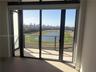 Floor-to-ceiling glass sliding doors opening to a covered balcony with a glass panel railing, tile flooring, and expansive panoramic scenery of a race