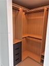 Custom walk-in closet featuring light wood-finish cabinetry, integrated linear LED lighting, dark matte drawers, and multiple hanging rods
