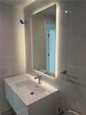 Wall-mounted vanity with integrated sink and single-handle faucet, backlit rectangular mirror, and large-format porcelain tile wall surround