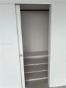 Storage space featuring a white sliding door, square chrome-finish hardware, three built-in shelves, and a horizontal hanging rod