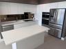 Kitchen featuring white high-gloss cabinetry, stone-surface countertops, a mirrored backsplash, stainless steel appliances, and a central island with 