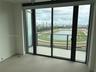 Floor-to-ceiling glass sliding doors, expansive balcony with glass railing, large-format tile flooring, and panoramic cityscape scenery