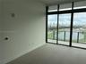 Floor-to-ceiling windows featuring panoramic city and water scenery, large-format tile flooring, and a private balcony with glass railing