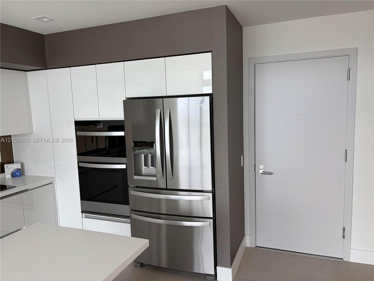 Kitchen featuring flat-panel white cabinetry, integrated stainless steel double wall ovens, a stainless steel French-door refrigerator, and solid-surf