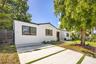 Stucco exterior featuring dark-framed windows, a concrete ribbon driveway with turf accents, and a horizontal slat privacy gate