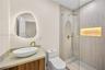 Bathroom featuring an asymmetrical backlit mirror, wood-finish vanity with a vessel sink, brass fixtures, glass-enclosed shower with tiled walls, and 