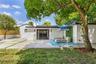 Rear exterior featuring a concrete patio, sliding glass doors, mature trees, a bamboo privacy screen, and exterior wall-mounted lighting